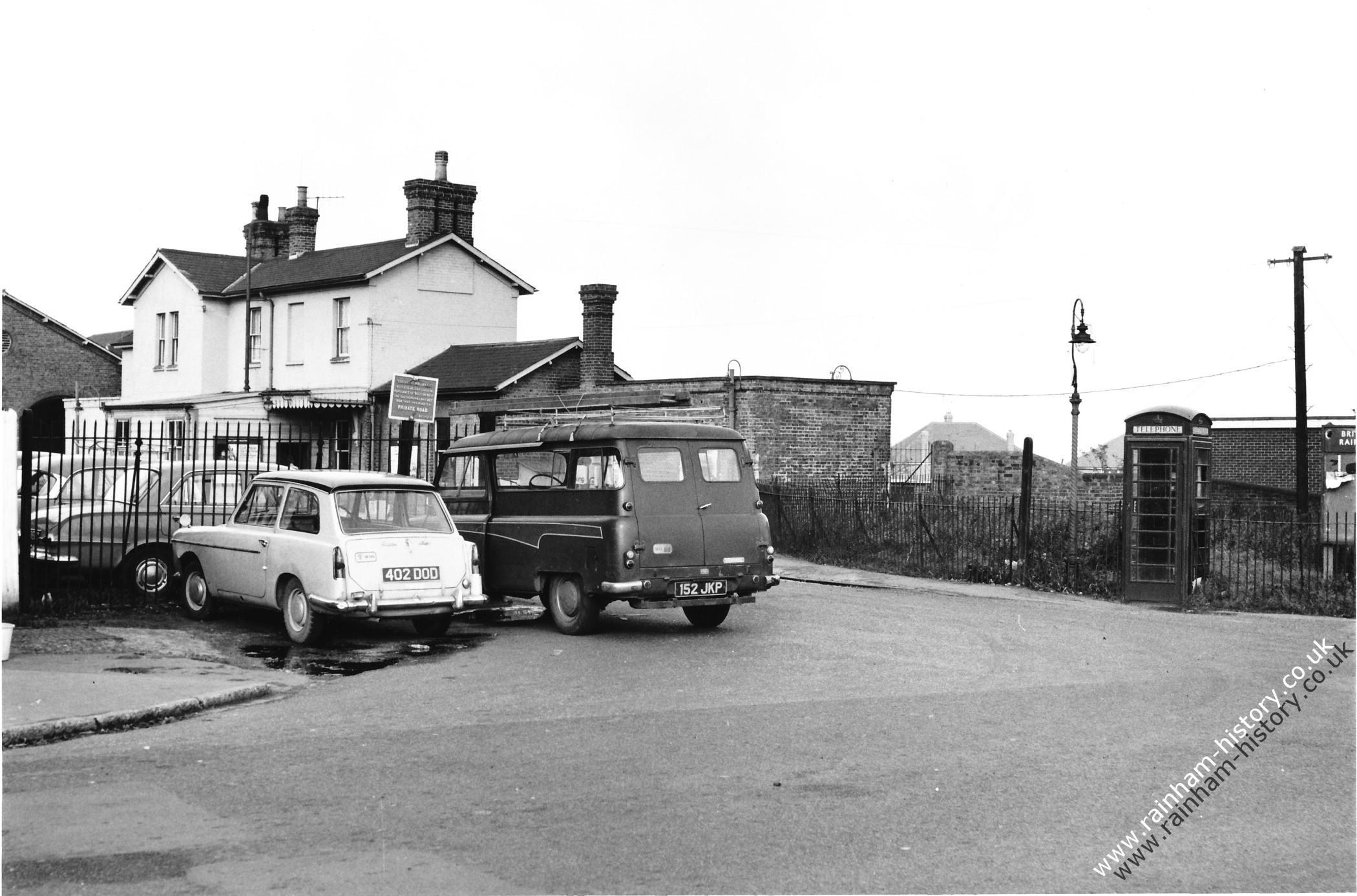 View of the station building from Station Road showing phone box on the corner. Multiple cars are visible in the picture, Austin A40 Farina registration 402DOD, Bedford CA van number plate 152 JKP. Over the railings is a Vauxhall Victor.